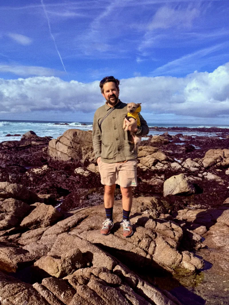 Andrew Ford on the California coast, holding a small dog